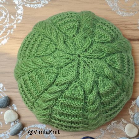 Hand-knitted green ribbed cable beanie showing top view after crown decreases, forming a neat star-shaped pattern.