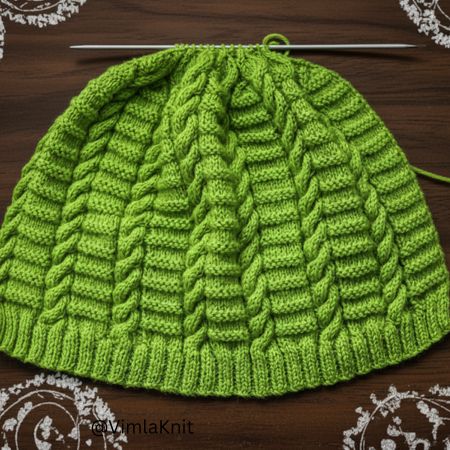Green ribbed cable beanie knitting pattern in progress on needles.