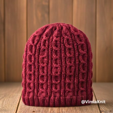Front view of maroon cable knit beanie hat with vertical twisted cable pattern and ribbed brim, handmade winter unisex hat displayed on a wooden background by Vimla Knit.