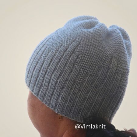Side profile of a person wearing a hand-knitted unisex light grey beanie featuring a skyline rib design and garter stitch crown against a clean, neutral background.