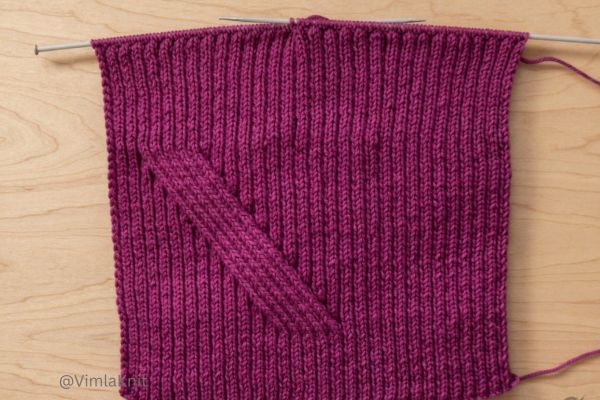 Close-up of hand-knitted purple ribbed beanie in progress on metal knitting needles, featuring classic 2X2 ribbing and diagonal shaping, perfect for beginners learning how to knit a hat.
