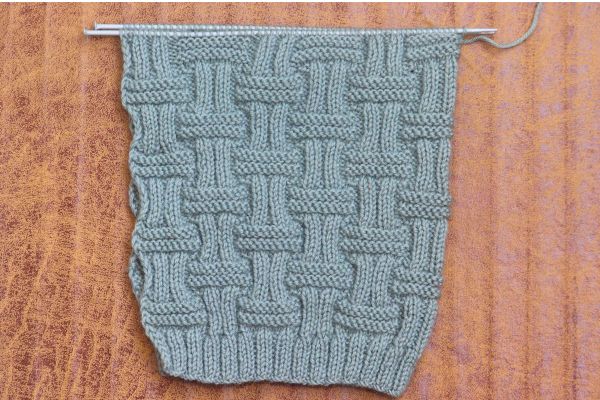 Sage green double basket rib stitch knitting swatch on straight needles showing beautiful basketweave cable pattern. Perfect for learning this easy textured stitch for unisex beanie.