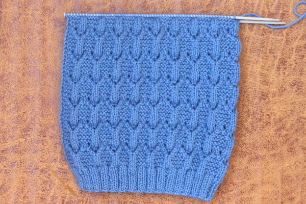 Blue lace knit beanie hat in progress on knitting needles showing diamond lace pattern and ribbed brim – Easy Knit Beanie Hat Pattern by Vimlaknit.