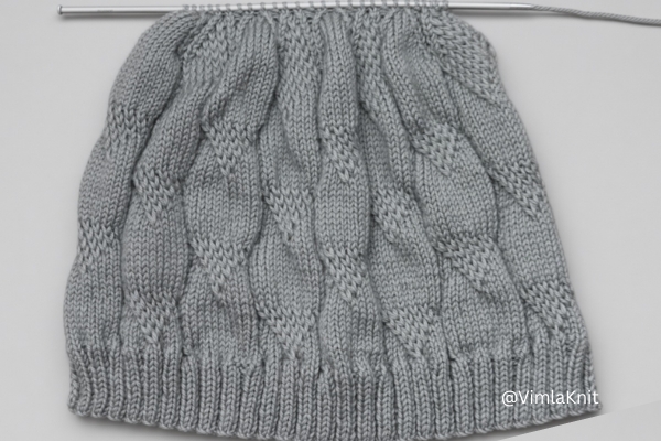 Gray cable beanie knit pattern on straight needles, crown decrease stage.