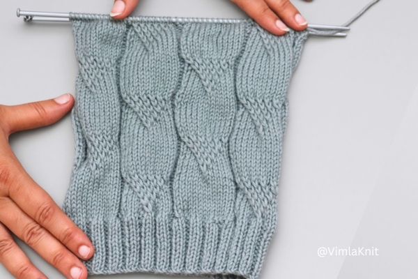Sage green hand knit cable pattern beanie, work in progress on straight needles.