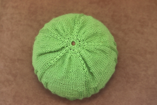 Top view of green knit beanie showing crown decrease shaping and center closure.